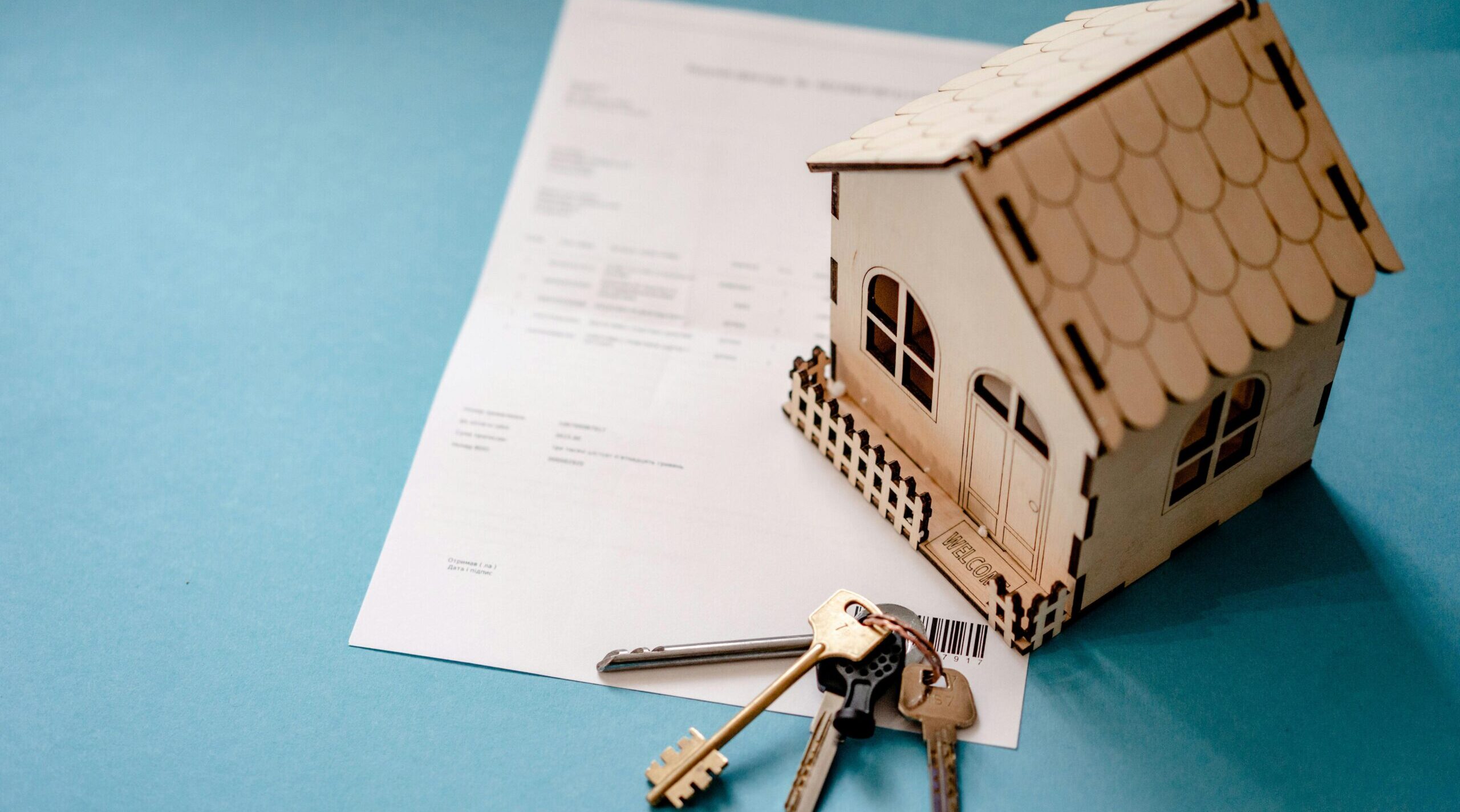 Contrato particular de compra e venda de imóveis com chaves e miniatura de casa sobre documento.