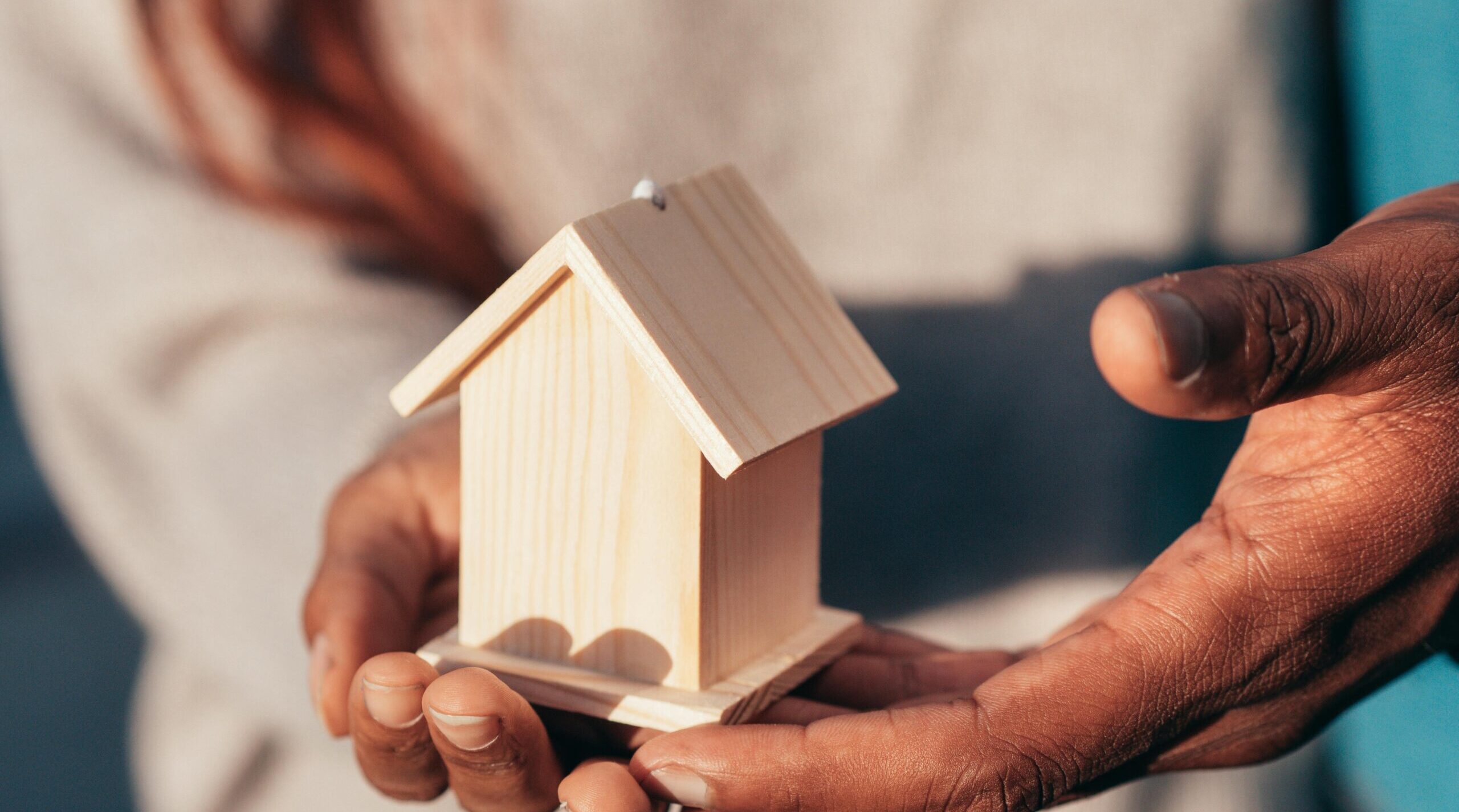 Pessoa segurando uma pequena casa de madeira nas mãos, simbolizando segurança e proteção nos contratos de locação.